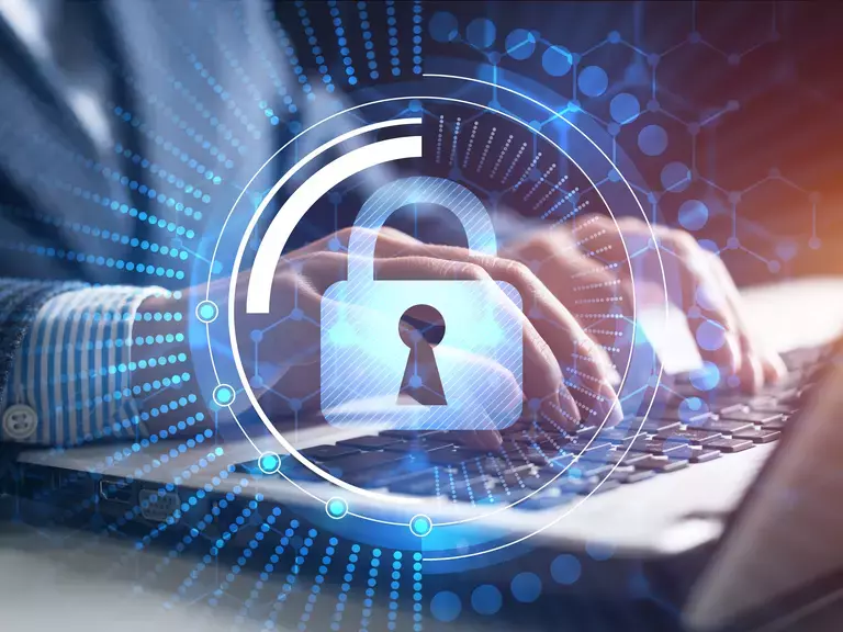 Hologramm eines Vorhängeschlosses als Symbol für das Schließen von Datenlecks mit Mann im Hintergrund, der auf einer Tastatur tippt.