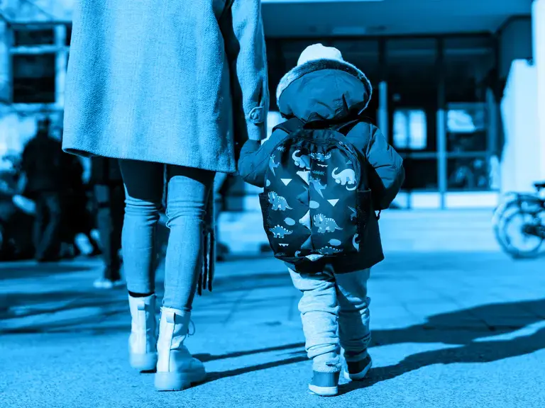 ein Mutter, die ihr Kind an der Hand hält und auf ein Gebäude zu geht