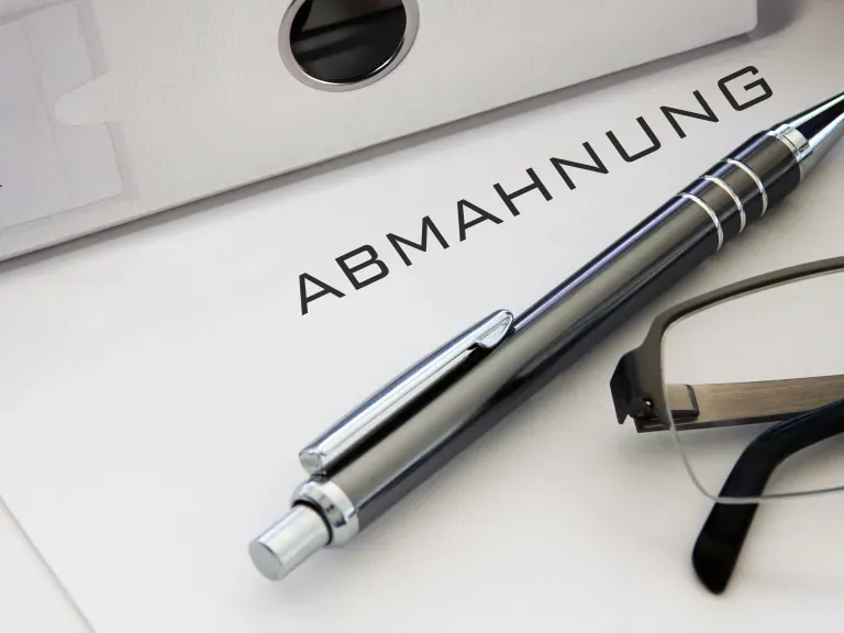 Ein Blatt auf dem Abmahnung steht, darauf liegen ein Stift und eine Brille