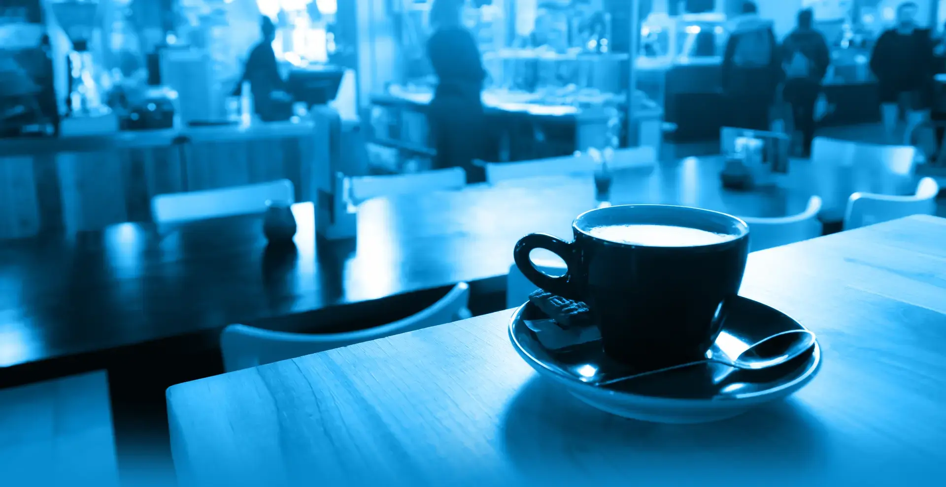Im Vordergrund eine Kaffeetasse auch einem Tisch in einem Café