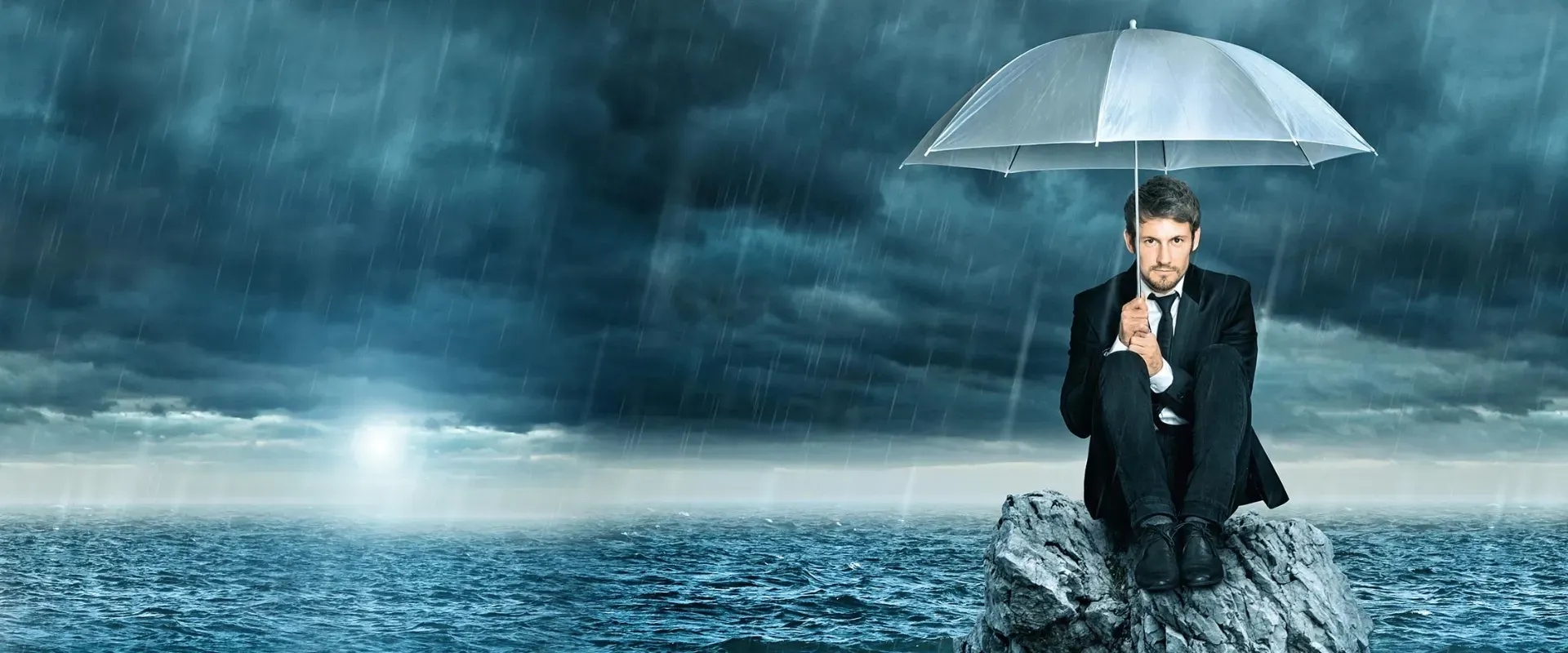 Ein Mann unter einem Regenschirm auf einem Stein um ihn herum Wasser