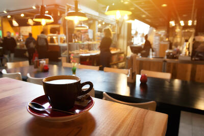 Kaffeetasse auf Holztisch mit verschwommener Gaststätte im Hintergrund.