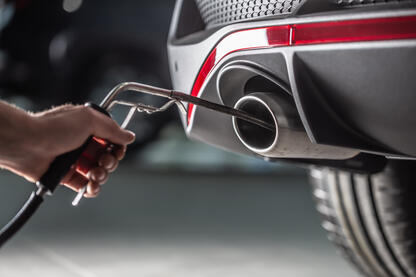 : Dieselskandal bei Hyundai &amp; Kia: Männliche Hand, die eine Sonde in den Auspuff eines Fahrzeugs hält, um die Abgasemission zu messen.
