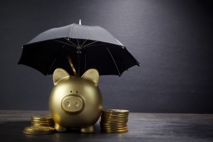 Ein goldenes Sparschwein mit Münzen daneben, das unter einem Schirm steht